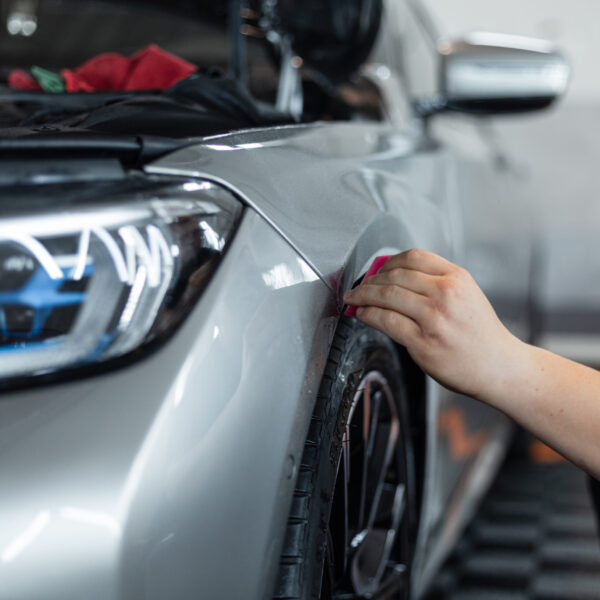 Professional man covers car with protective film and cuts with b Professional man covers car with protective film and cuts with blade in detailing service. Car protection and care